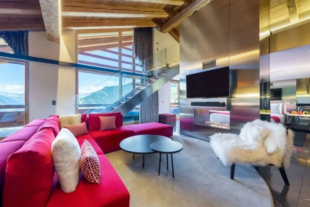 Modernes Wohnzimmer der WOW Suite mit rotem Sofa, Designertreppe und großem Fenster.