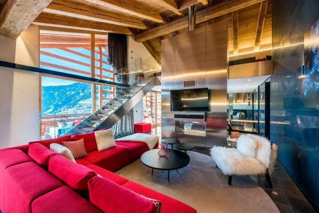Geräumiges Wohnzimmer in der WOW Suite mit roten Sofas, großer Treppe und Bergblick.
