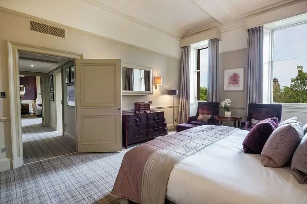 Elegantes Doppelzimmer mit bequemen Sesseln und großen Fenstern mit Blick auf die Stadt.