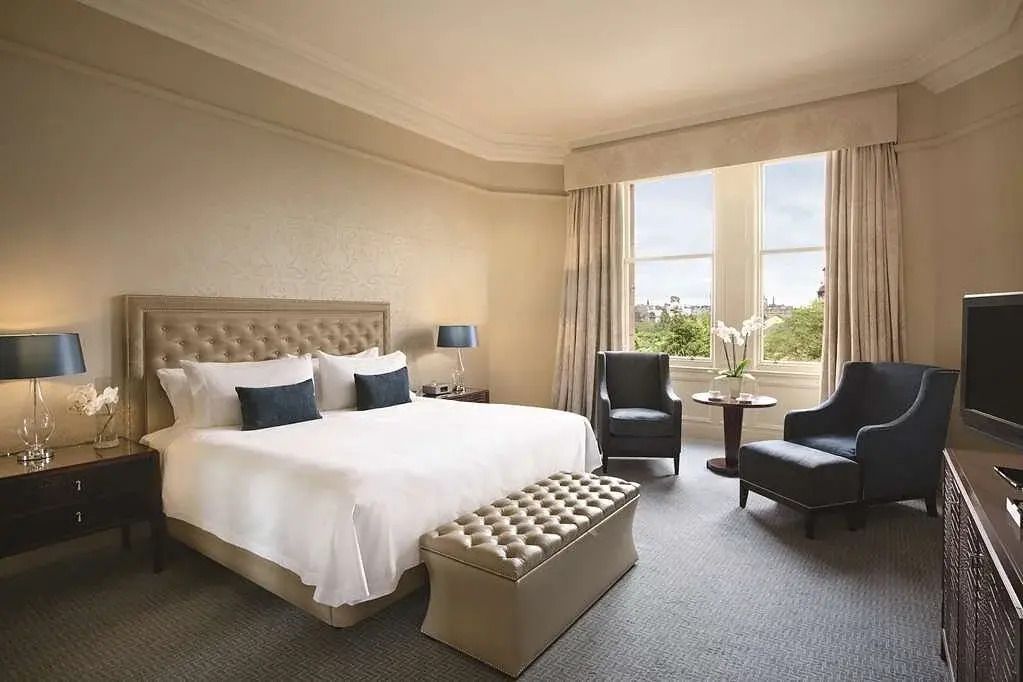 Elegantes Schlafzimmer mit großem Bett, Sesseln und großen Fenstern mit Stadtblick