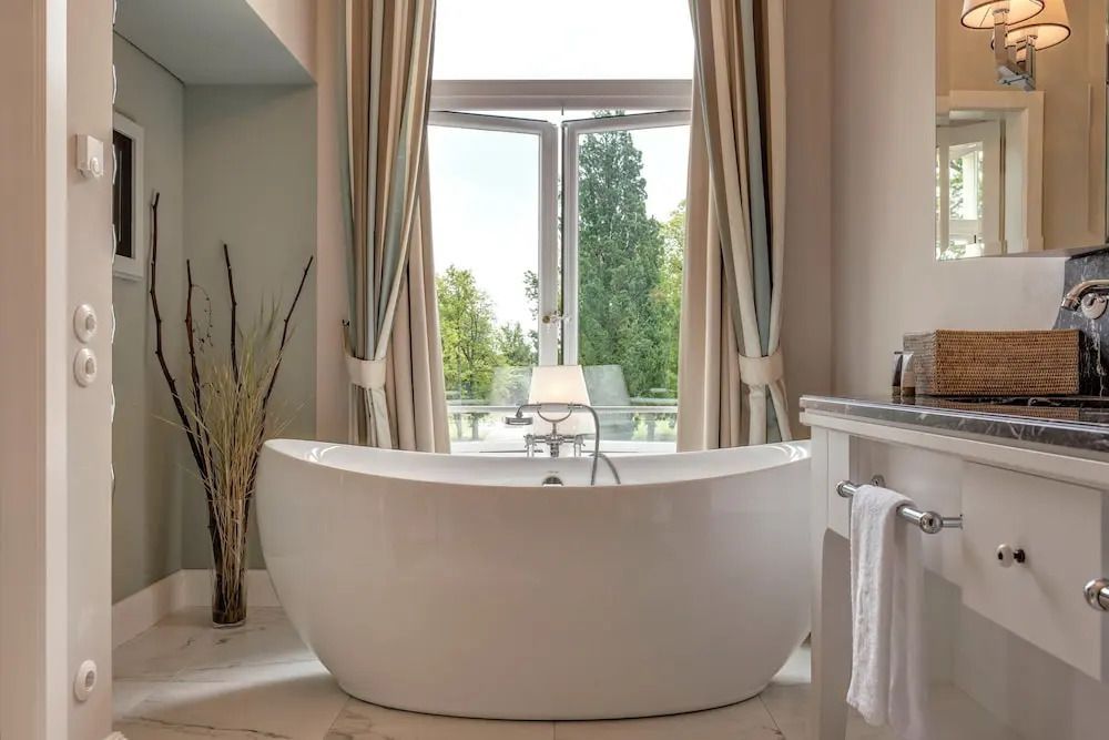 Luxuriöse freistehende Badewanne mit Blick durch großes Fenster auf grüne Landschaft
