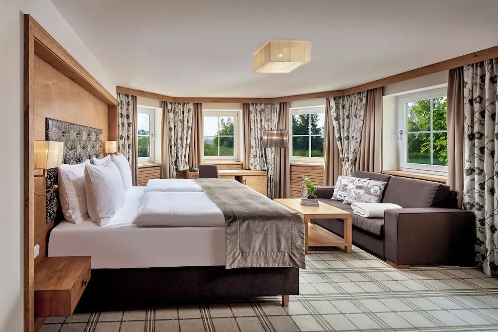 Geräumiges Zimmer mit Doppelbett, Sofa und großen Fenstern mit Blick ins Grüne