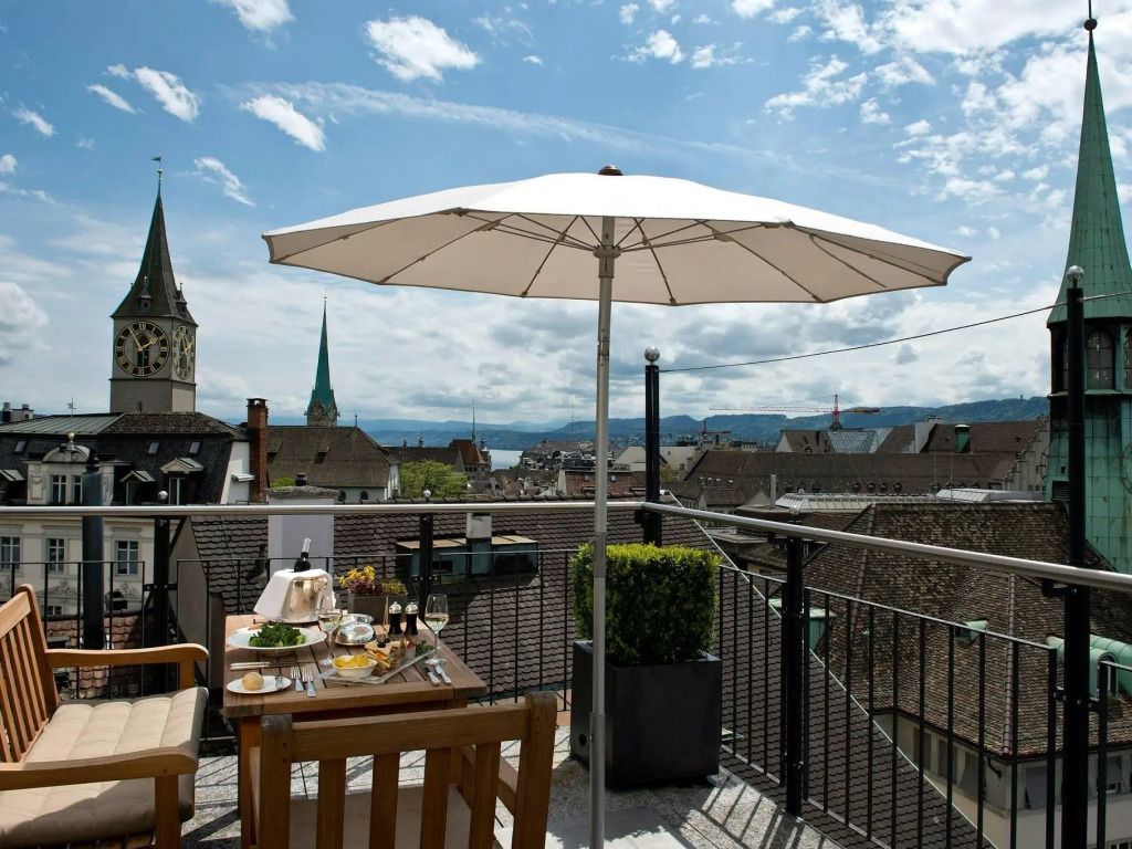 Dachterrasse mit Blick über die Stadt und gedecktem Tisch unter einem Sonnenschirm