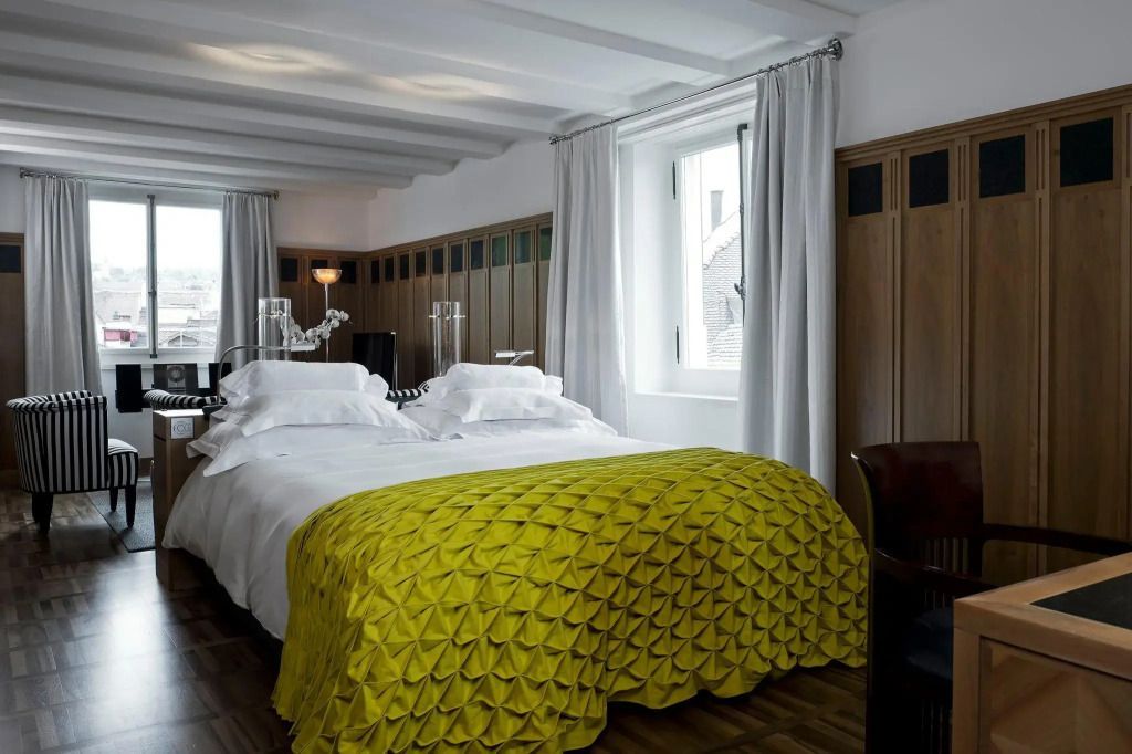 Design-Doppelzimmer mit weißer Bettwäsche und gelber Decke, Holzpaneele, Fenster.