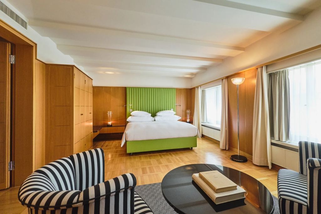 Geräumiges Zimmer mit grünem Kopfteil und gestreiftem Sessel