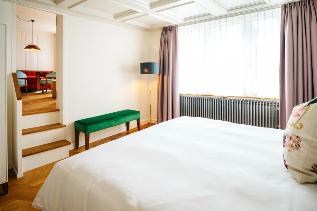 Helles Schlafzimmer mit weißem Bett und grünem Sitzbank am Fenster
