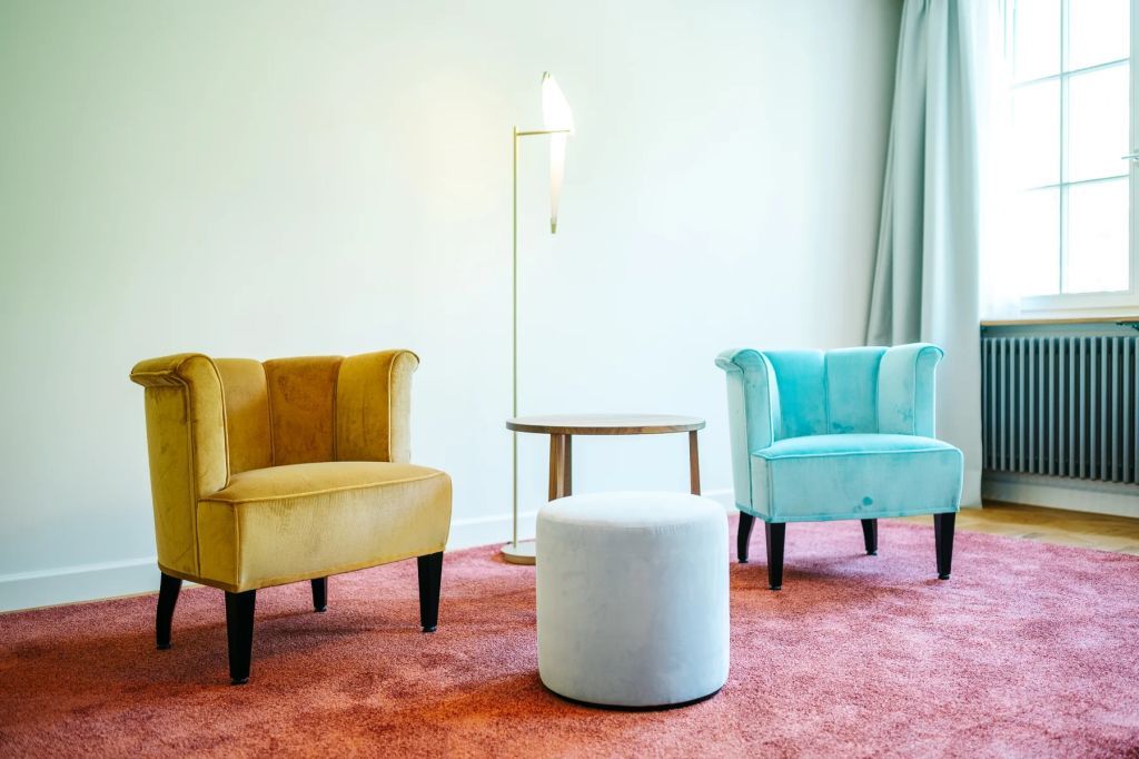 Zwei bunte Sessel mit rundem Tisch auf rosa Teppich