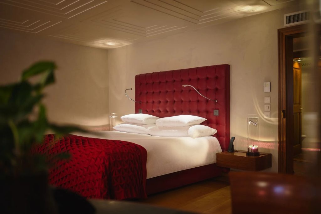 Luxuriöses Doppelzimmer mit rotem Kopfteil und dezenter Beleuchtung.