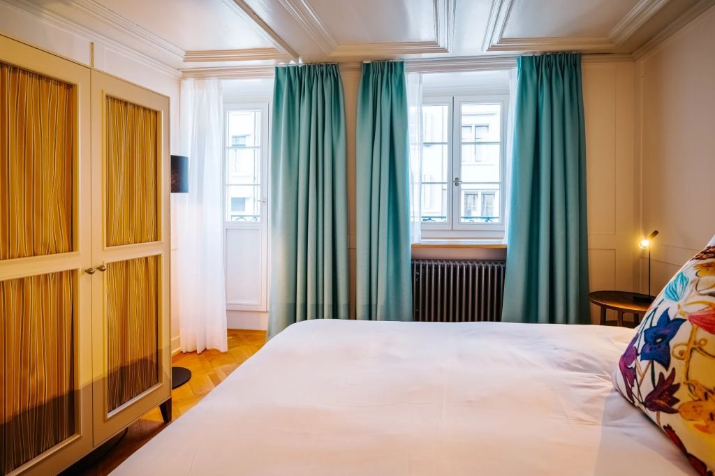 Helles Schlafzimmer mit großen Fenstern und türkisfarbenen Vorhängen
