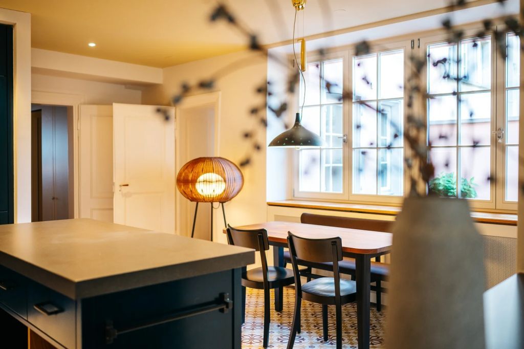 Offener Raum mit Esstisch und origineller Lampe neben großen Fenstern