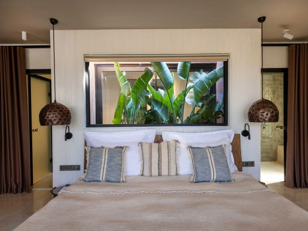 Modernes Schlafzimmer mit großem Bett und Aussicht auf tropische Pflanzen.