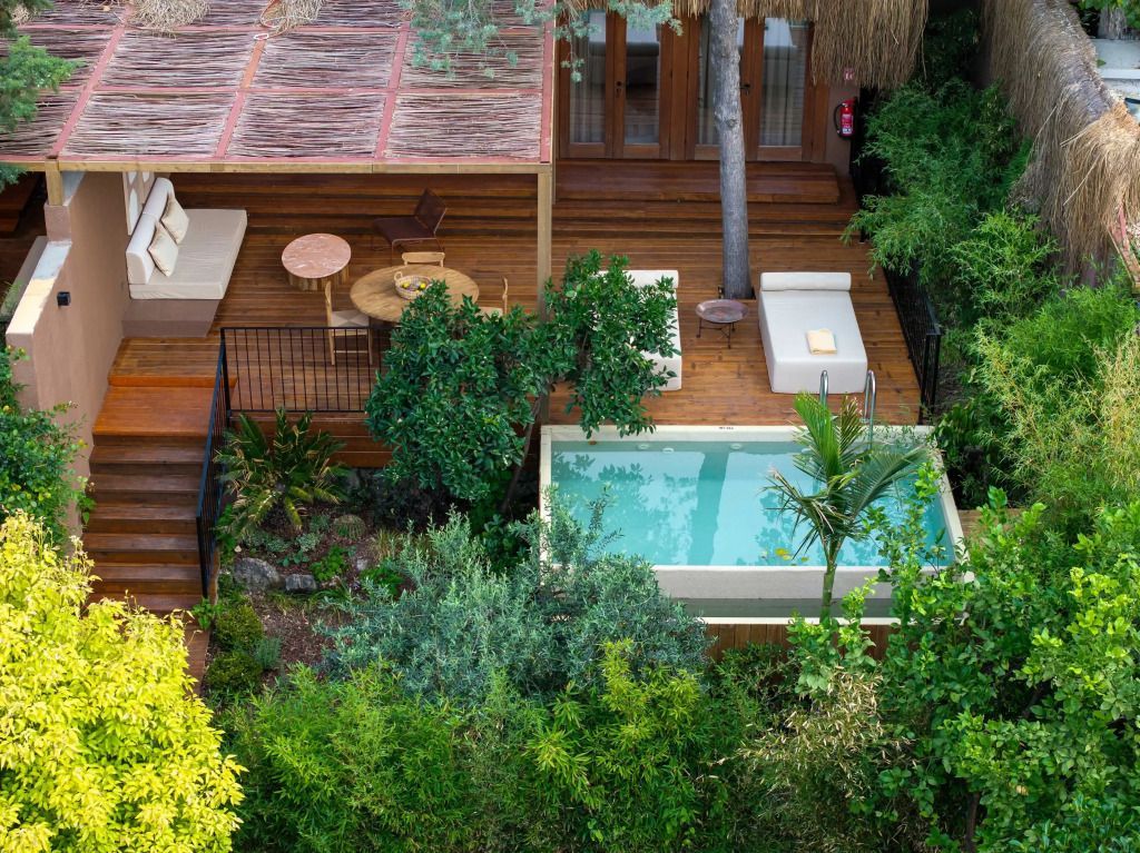 Holzterrasse mit kleinem Pool umgeben von üppigem Grün.