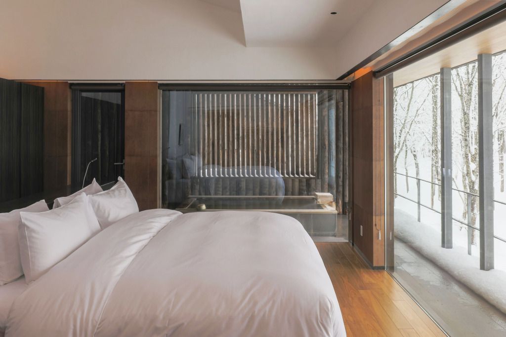 Helles Doppelzimmer mit großem Bett und Fensterwand, wodurch Naturblick ermöglicht wird.