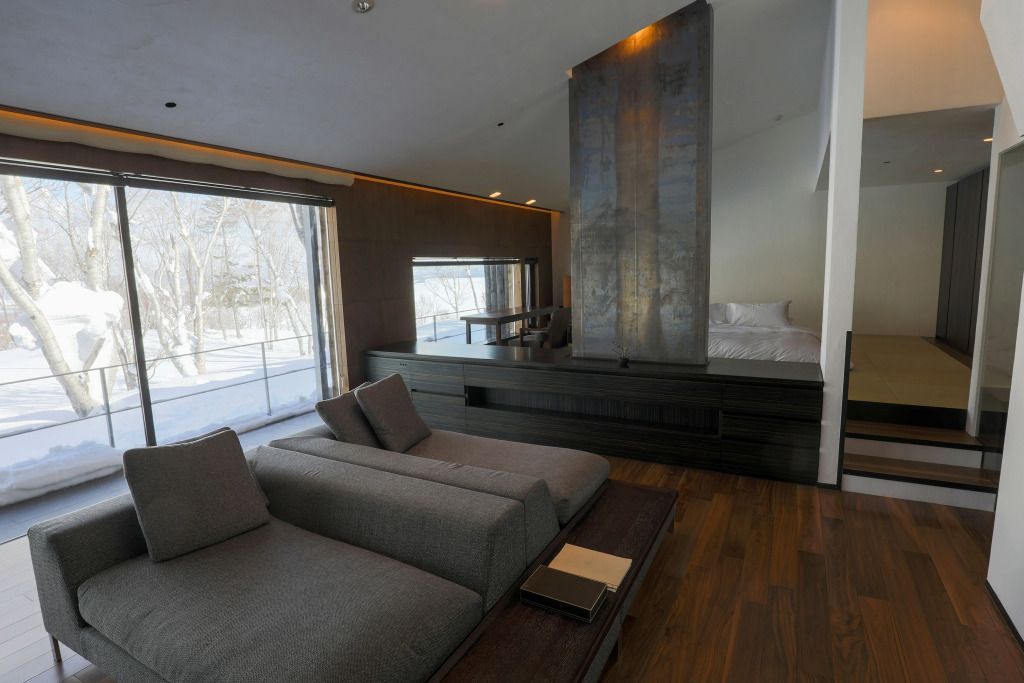 Modernes Zimmer mit Sitzecke und großen Fenstern. Helle Holzelemente dominieren.