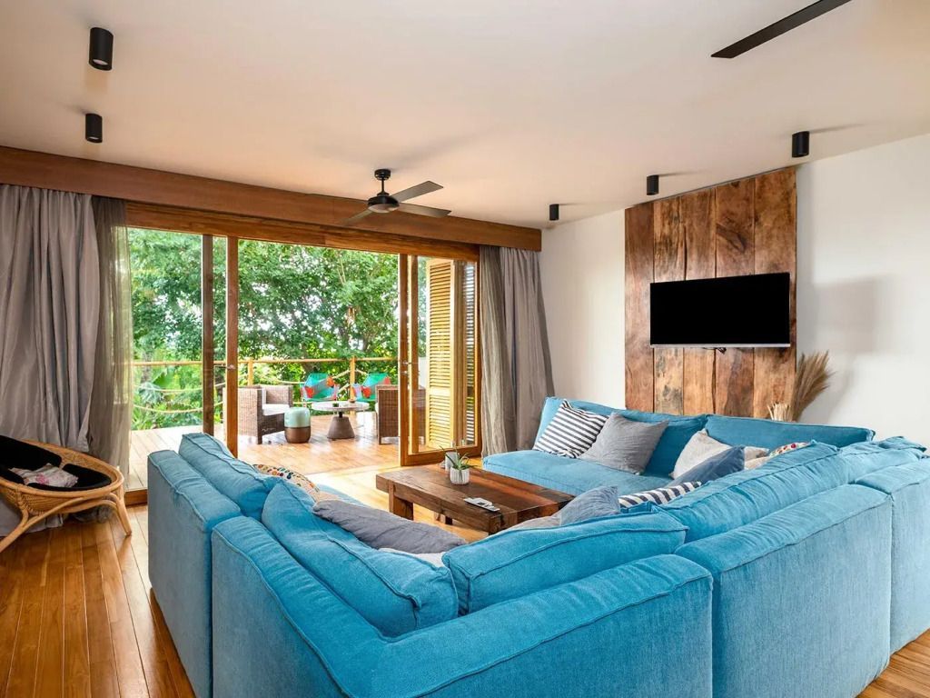 Gemütliches Wohnzimmer mit blauer Couch und Zugang zum Balkon mit Blick ins Grüne