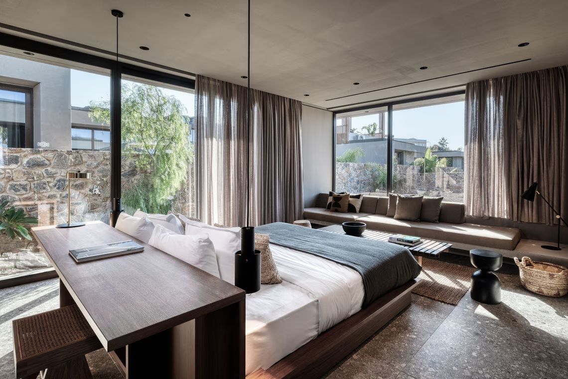 Modernes Hotelzimmer mit Doppelbett, Blick durch große Fensterfronten und integriertem Sitzbereich.