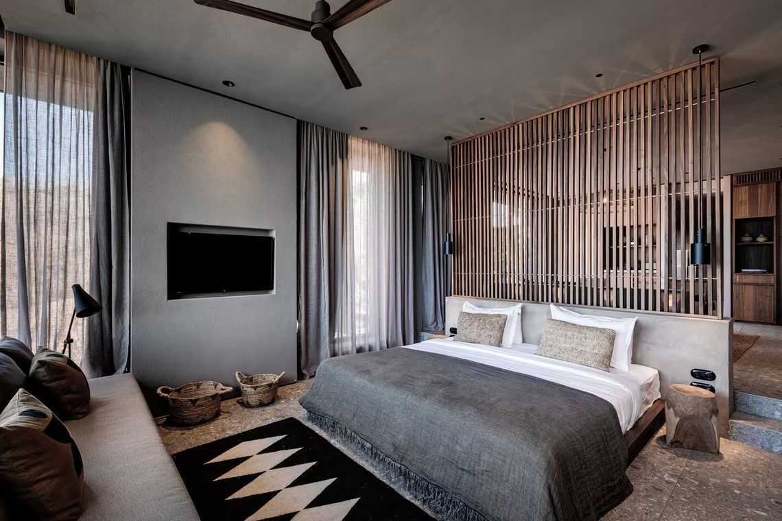 Modernes Hotelzimmer mit Doppelbett, Flachbildfernseher an grauer Wand und Holzlamellentrennwand.