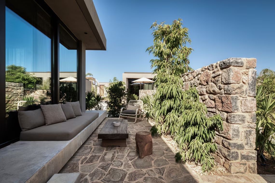 Terrasse aus Naturstein mit Sitzbank, Holzmöbeln und einer Steinmauer