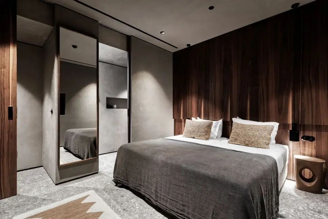 Modernes Hotelzimmer mit Doppelbett, dunkler Holzwand und großem Ganzkörperspiegel.