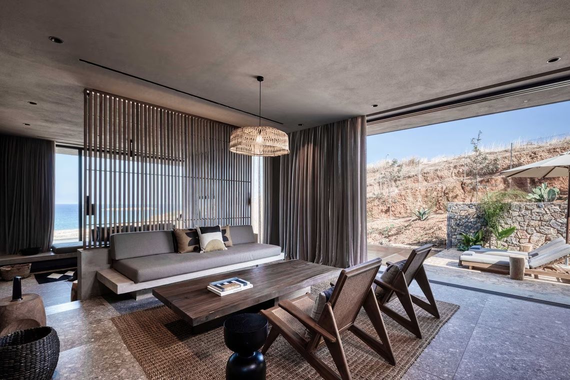 Wohnbereich einer Suite mit Sofa, Holztisch, Sesseln und großer Glasfront zur Terrasse.