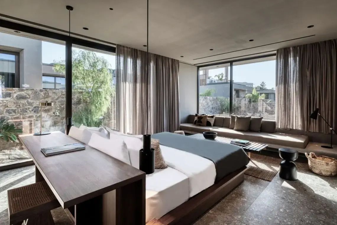 Lichtdurchflutetes Hotelzimmer mit Doppelbett, Sitzbereich und großen Fensterfronten.