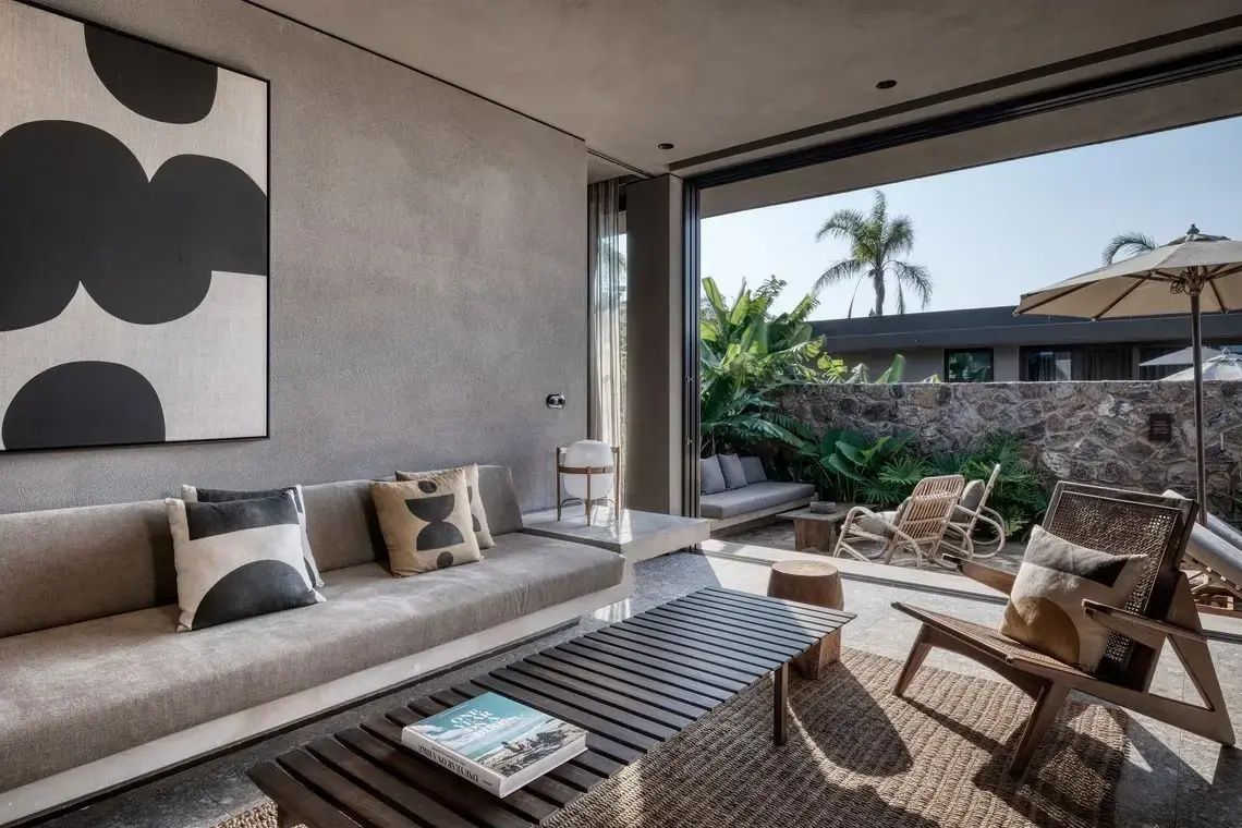 Offener Wohnbereich mit grauem Sofa, Holzcouchtisch und Zugang zur bepflanzten Terrasse.