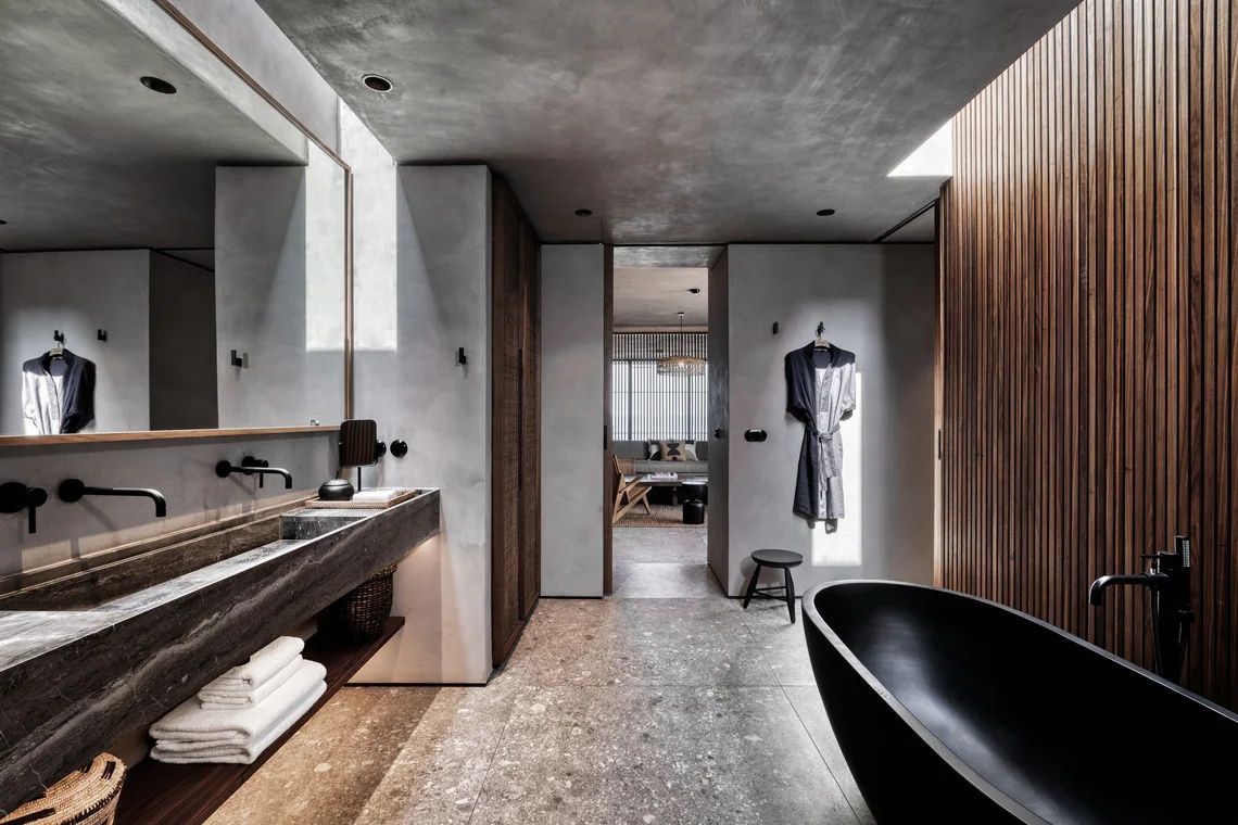 Badezimmer mit schwarzer freistehender Badewanne, Naturstein-Waschtisch und Handtüchern.