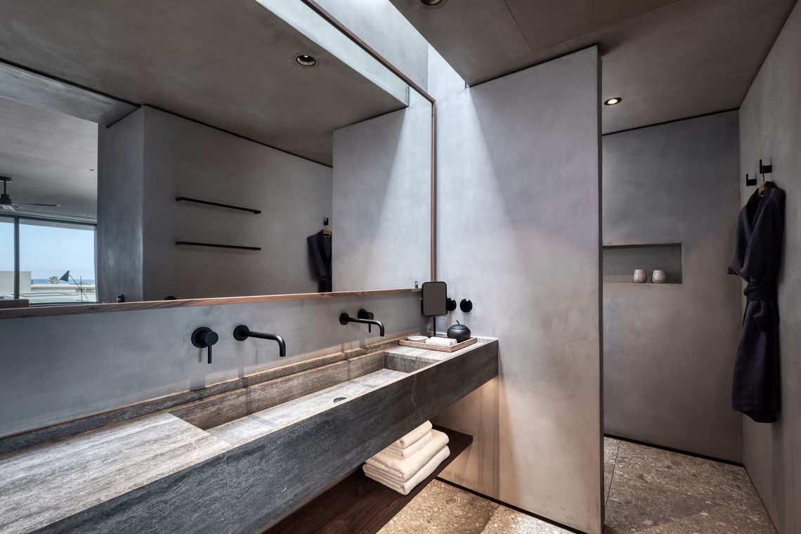 Modernes Badezimmer mit Waschtisch aus Stein, schwarzen Armaturen und großem Spiegel.