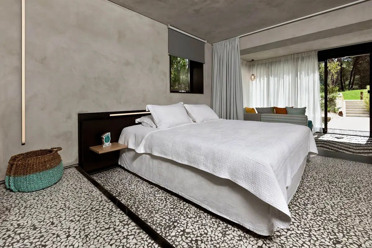 Doppelbett mit weißer Bettwäsche in einem modern gestalteten Hotelzimmer mit Terrazzoboden.