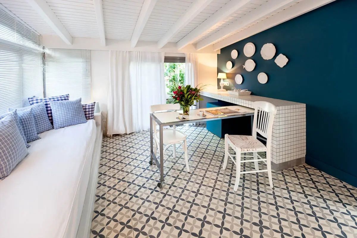 Wohnbereich mit Tisch, weißen Stühlen, gemustertem Fliesenboden und blauer Wand mit Tellerdekoration.