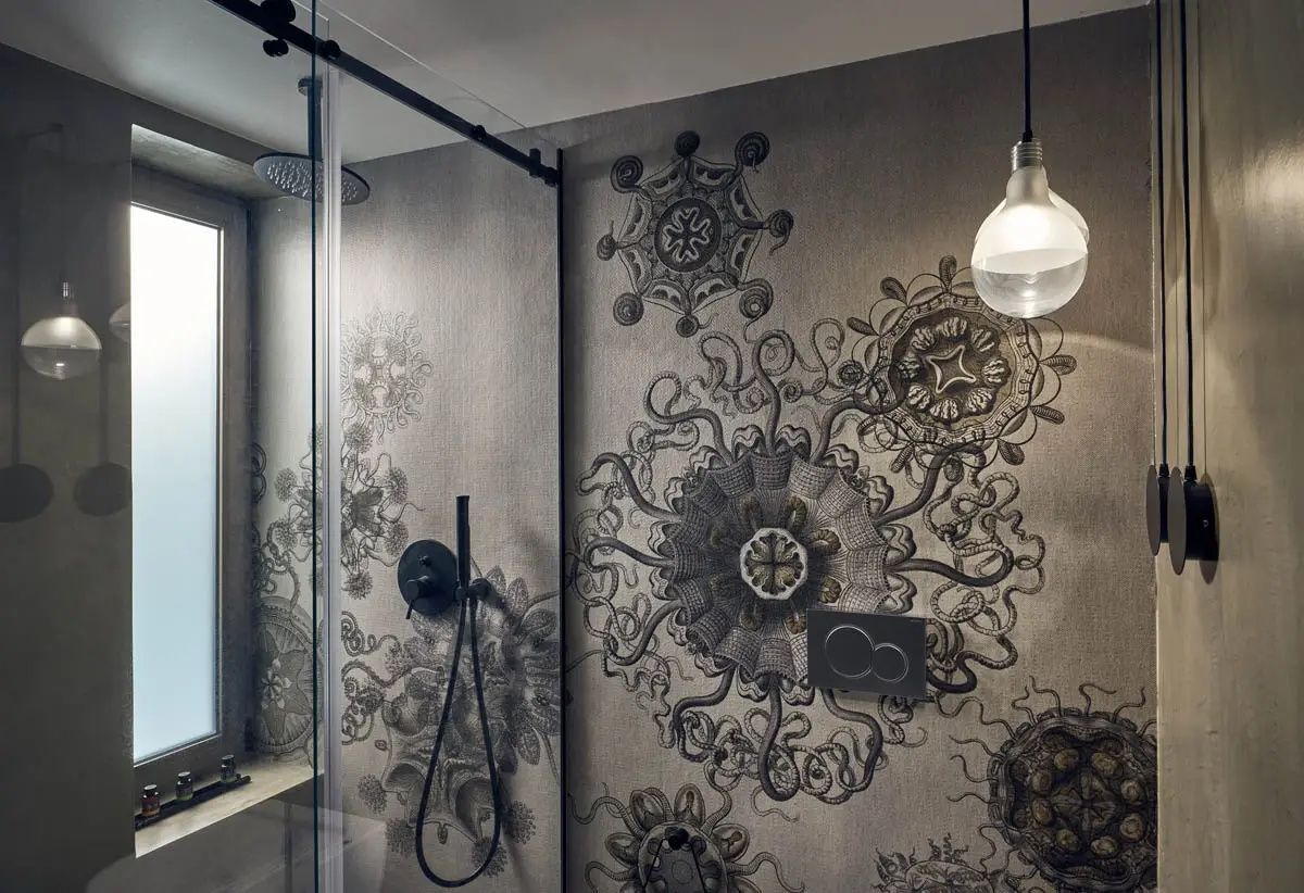 Badezimmer mit gemusterter Wandgestaltung, Dusche mit Glaswand und Hängeleuchte.