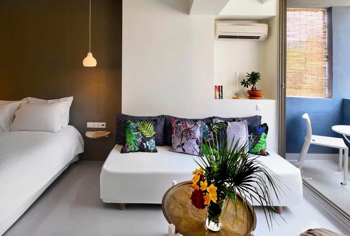 Sitzecke in einem Hotelzimmer mit weißem Sofa, bunten Motivkissen und Blumenstrauß auf dem Tisch.