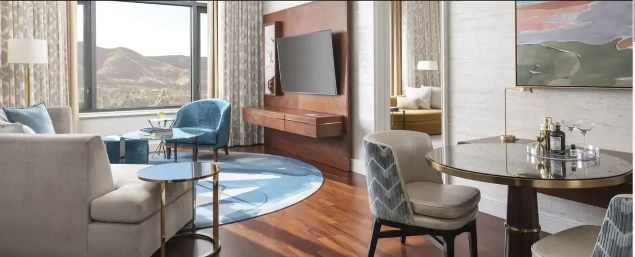 Modernes Hotelzimmer mit Holzfußboden, flachem Fernseher an einer Holzwand und blauem rundem Teppich.