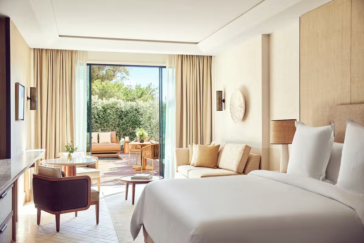 Helles Hotelzimmer mit Doppelbett, Sofa und Zugang zur privaten Terrasse im Grünen.