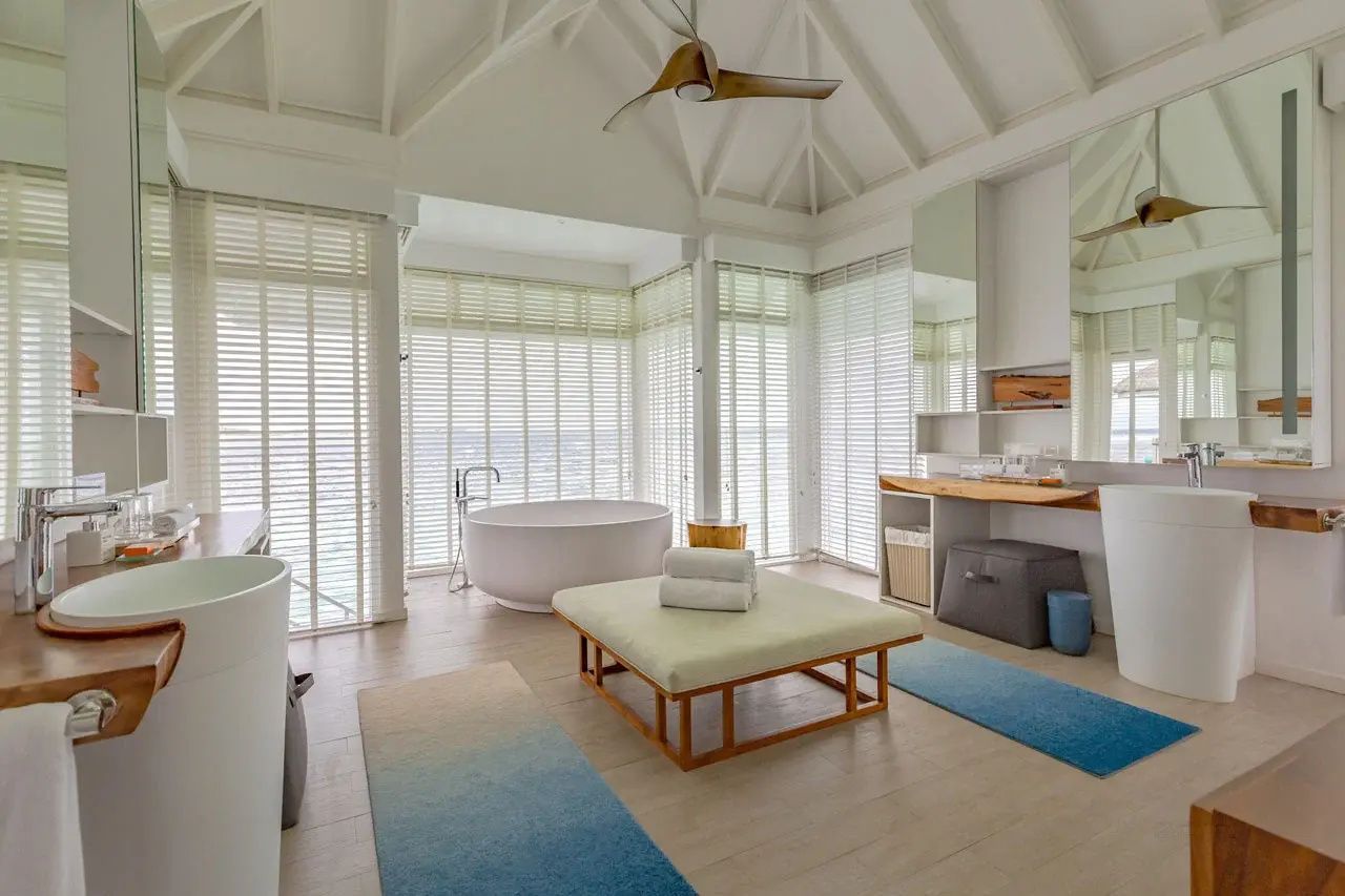 Großzügiges Badezimmer mit freistehender Badewanne und Blick auf das Meer durch Lamellen.