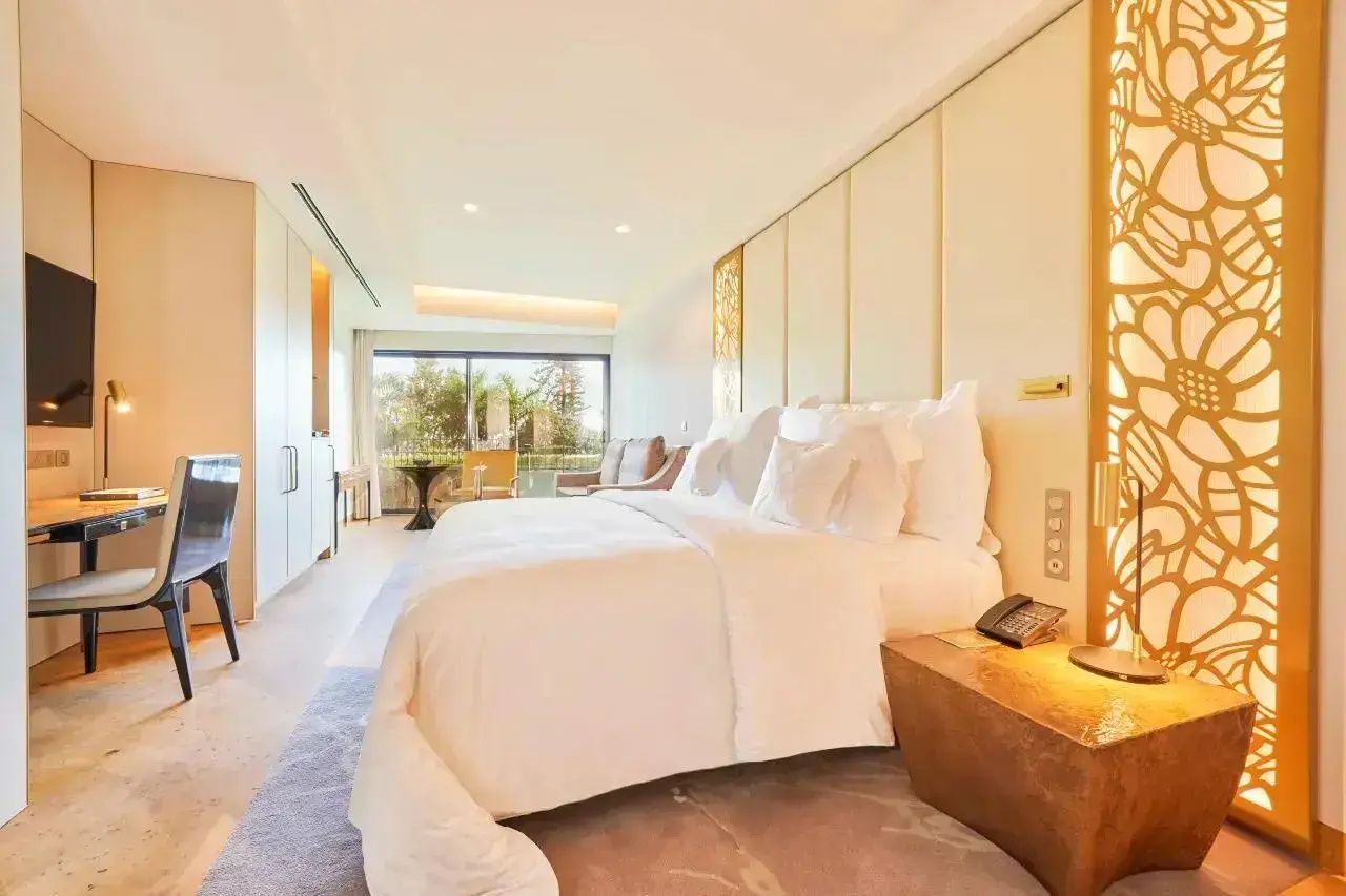 Heller Hotelraum mit großem Doppelbett, Nachttisch aus Holz und Balkonzugang mit Blick ins Grüne.