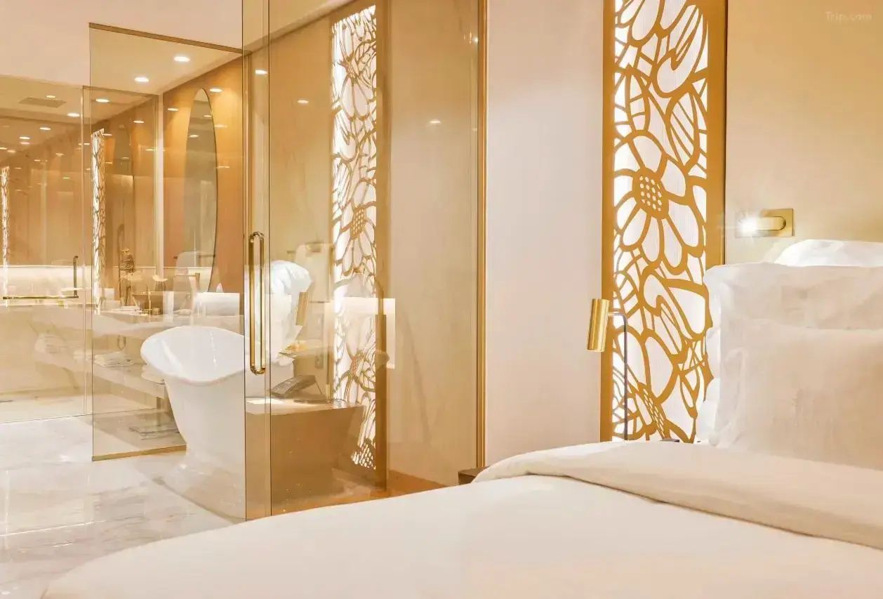 Blick vom Bett durch eine durchsichtige Glaswand auf eine freistehende Badewanne im Bad.
