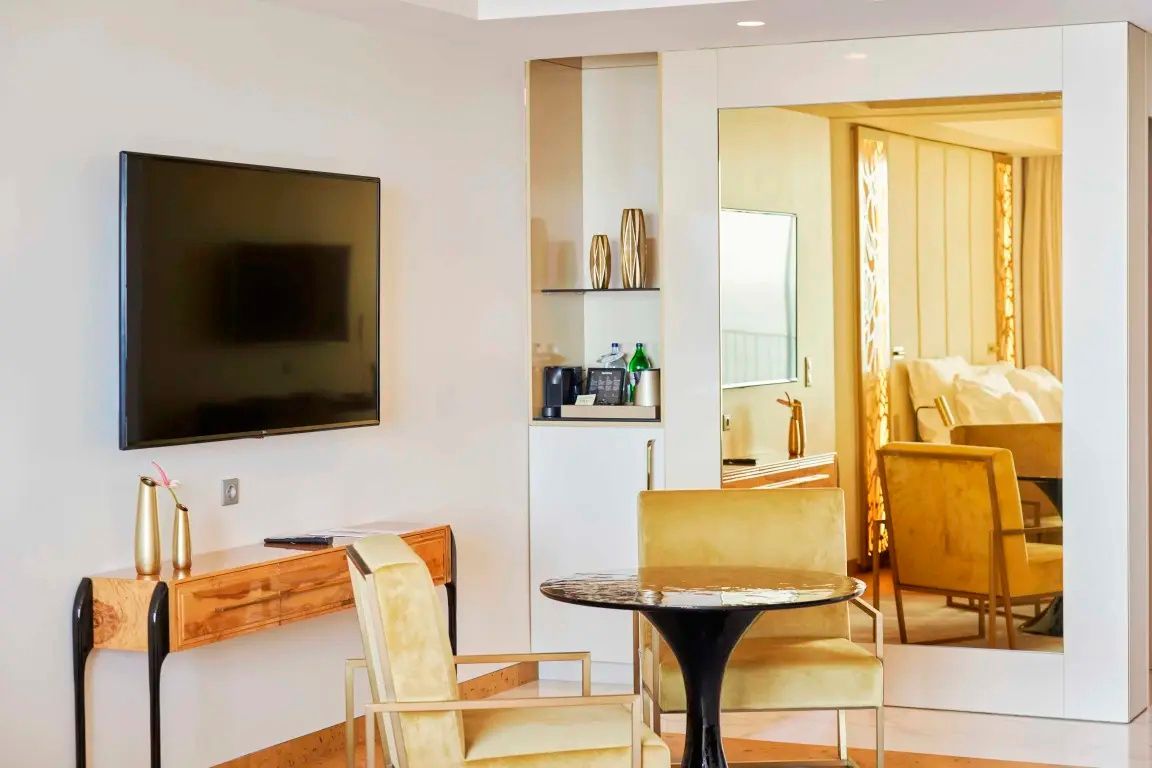 Sitzbereich im Hotelzimmer mit zwei gelben Sesseln, rundem Tisch und Fernseher an der Wand.