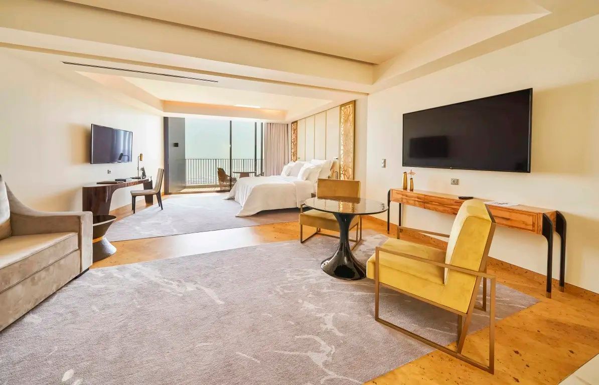 Übersicht des Hotelzimmers mit Doppelbett im Hintergrund, Sitzbereich und Zugang zum Balkon.