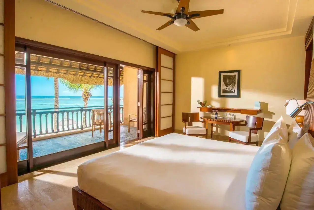 Helles Hotelzimmer mit Doppelbett, Deckenventilator und geöffneter Balkontür mit Blick auf den Ozean.