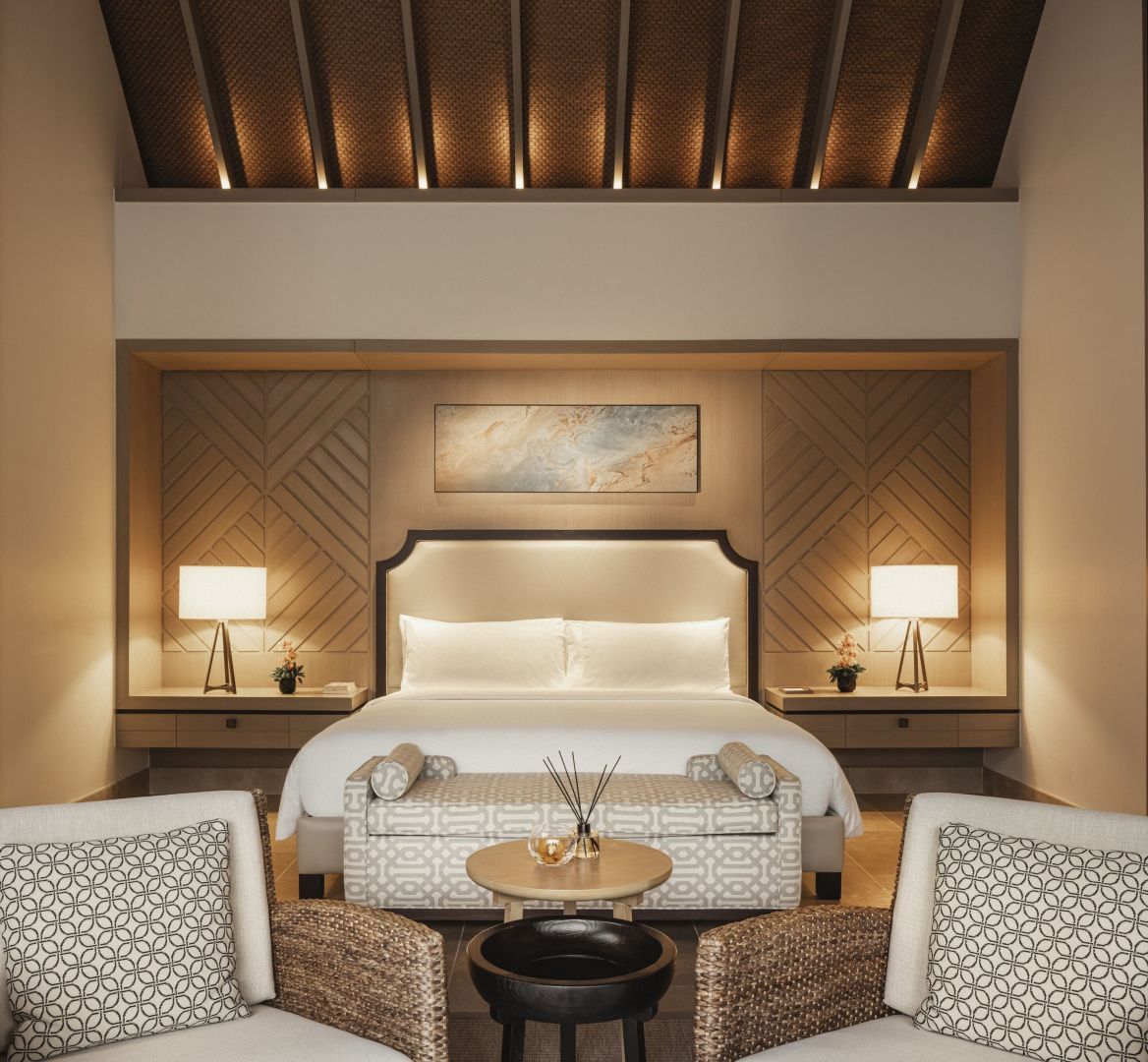 Helles Hotelzimmer mit großem Doppelbett, Wandbild und zwei Sesseln am Tisch.