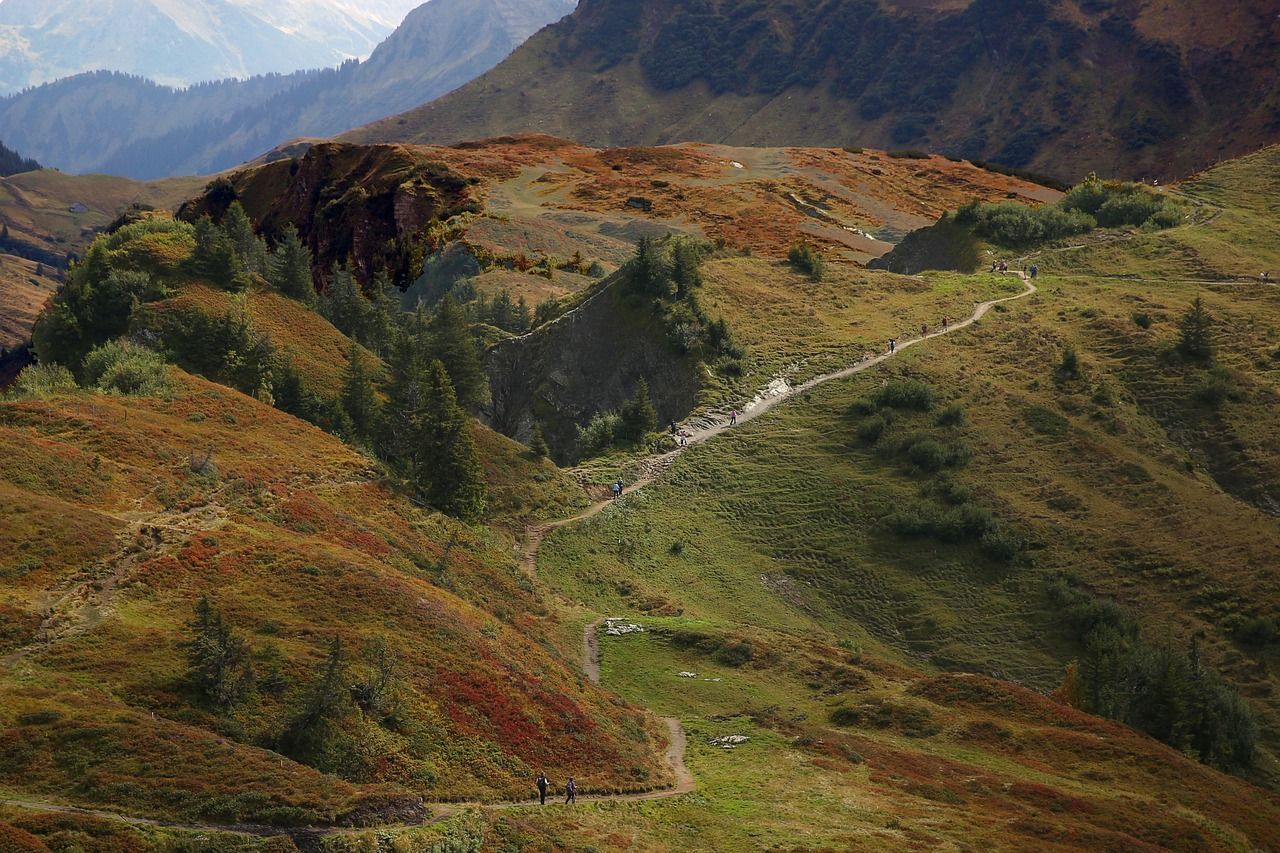 Gewundener Wanderweg durch grüne und rötliche Hügellandschaft.