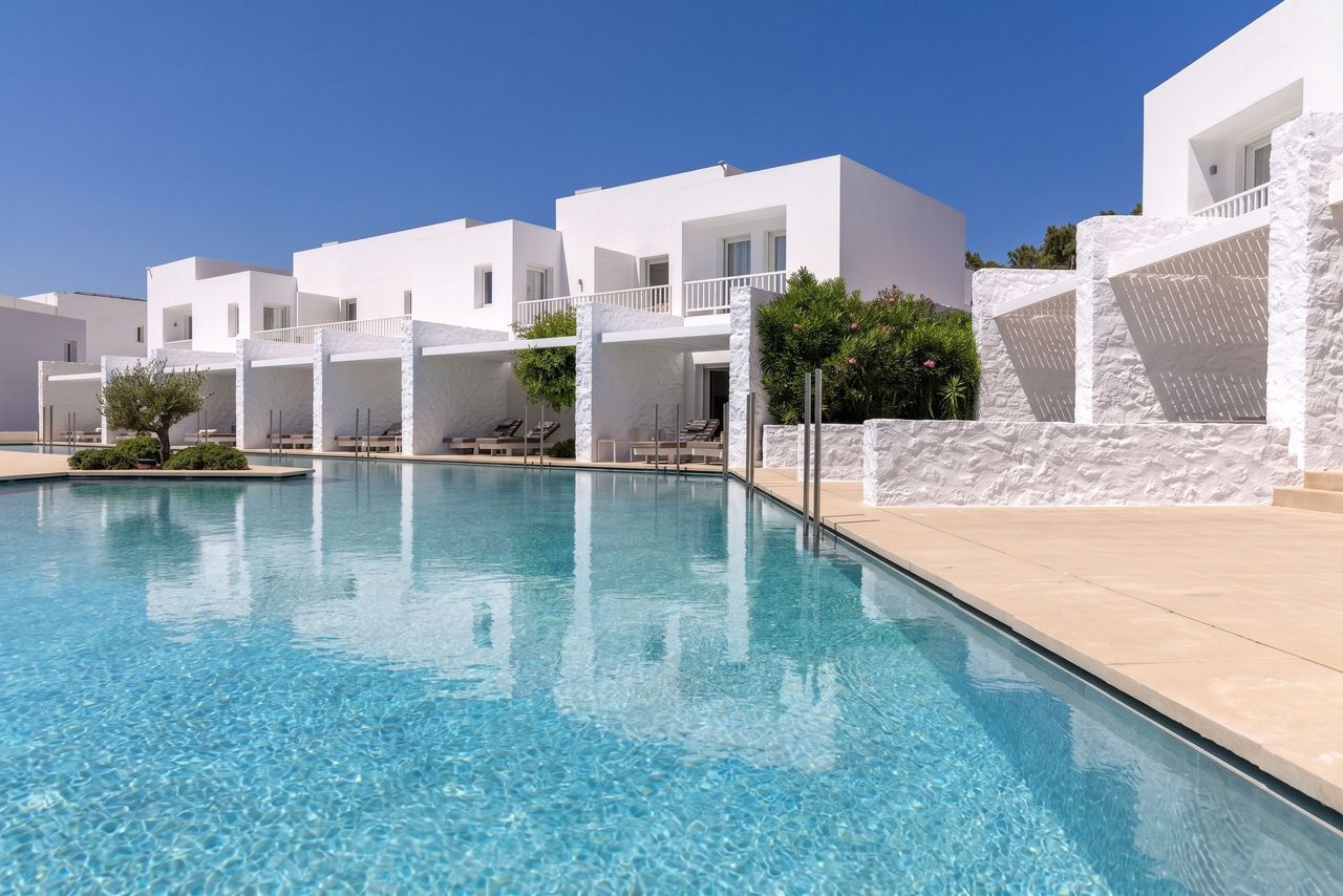 Strahlend weiße Resort-Architektur im kykladischen Stil mit großzügigem Swimmingpool und Sonnenliegen.