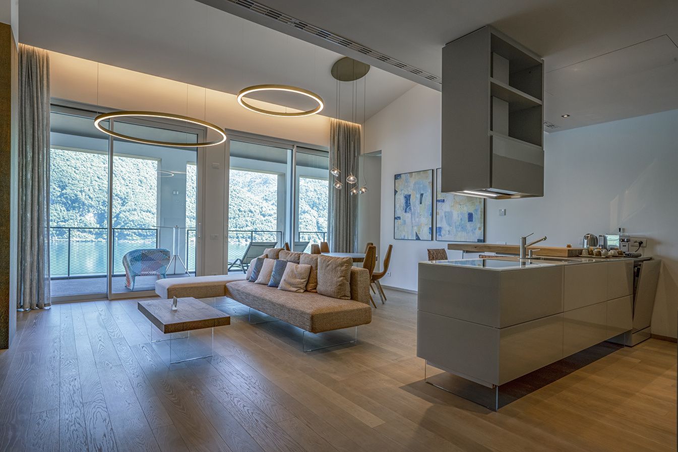 Offener Wohnbereich mit hellem Sofa, Holzboden und großer Fensterfront zum See.