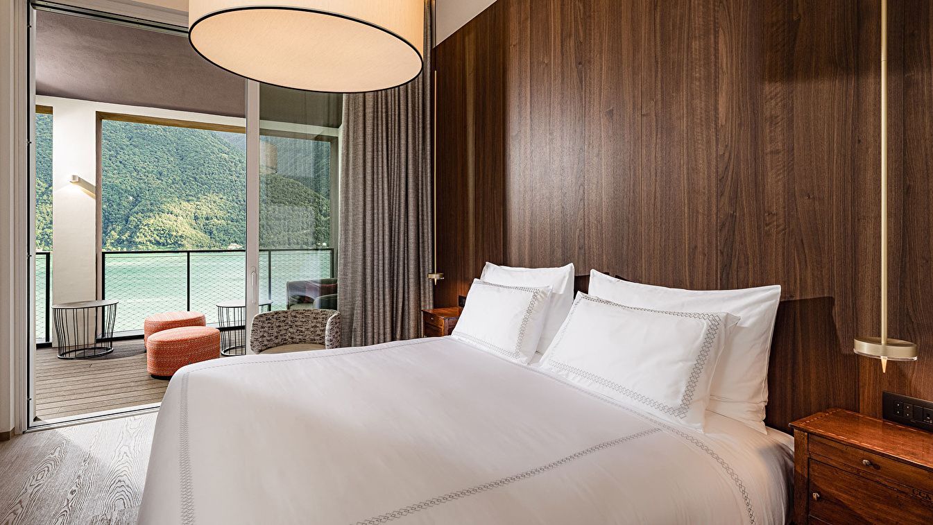 Doppelbett mit weißen Kissen vor einer dunklen Holzverkleidung und Blick auf den Balkon.