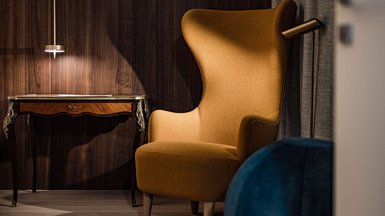 Gelber Ohrensessel neben einem kleinen hölzernen Beistelltisch im Hotelzimmer.