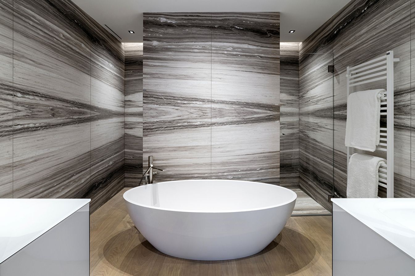 Freistehende runde Badewanne vor einer grau gemusterten Natursteinwand.