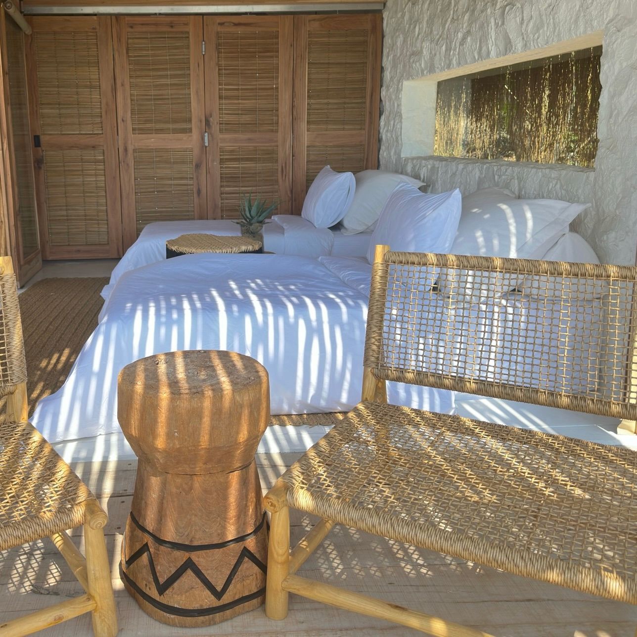 Holzzimmer mit Sofa, weißen Kissen und zwei geflochtenen Stühlen.
