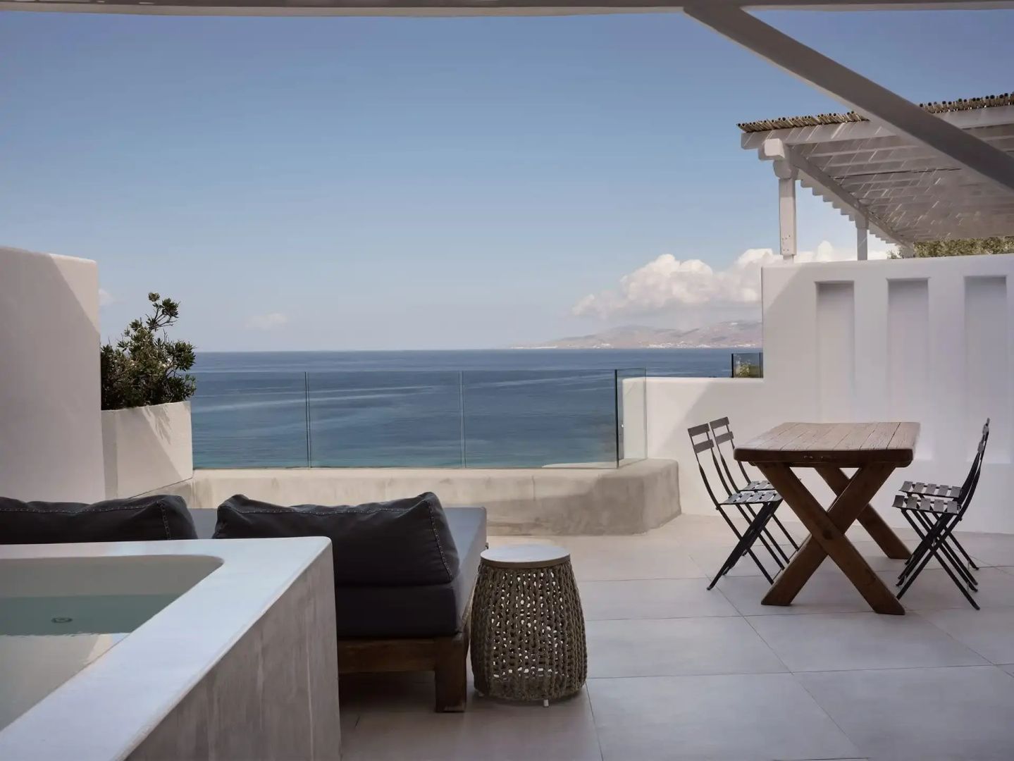 Terrasse mit Holztisch und Liegemöglichkeit mit freiem Blick auf das blaue Meer.