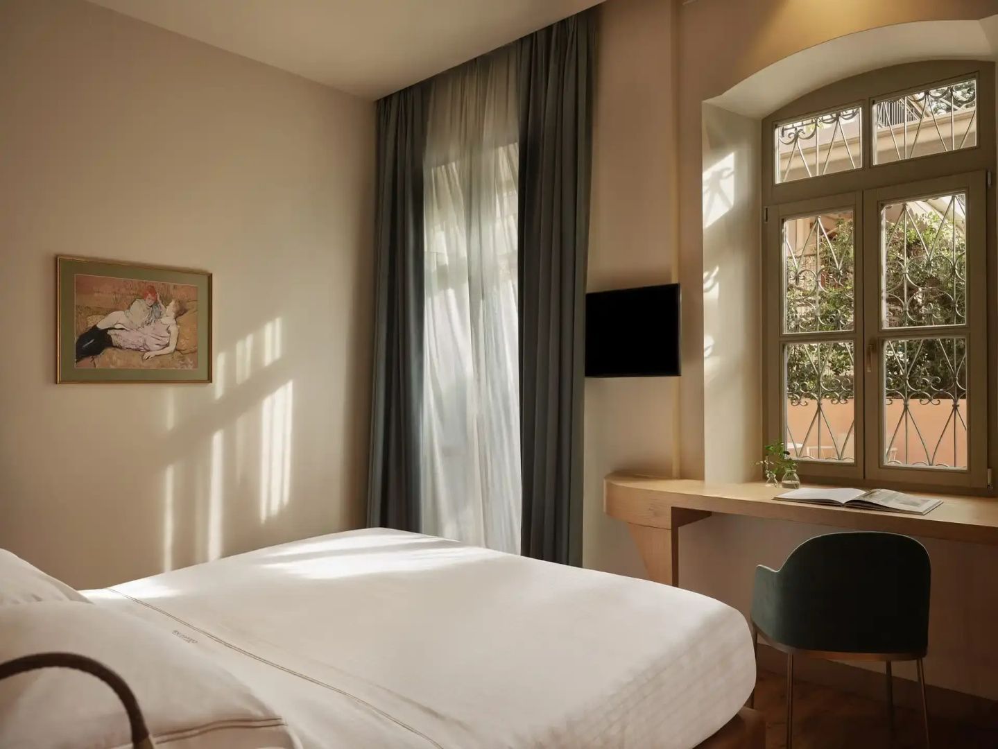 Helles Hotelzimmer mit Doppelbett, Wand-TV und Schreibtisch am Fenster.